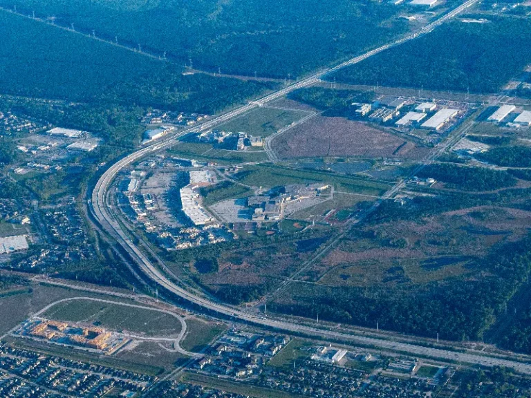 Aerial view of a suburban area with highways, buildings, and patches of forest.