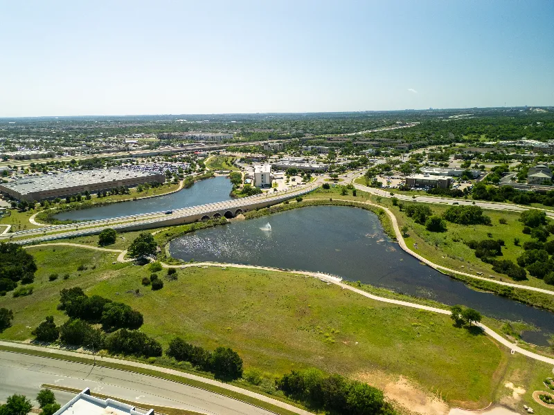 Aerial view of a park with two ponds, a bridge, walking paths, and surrounding urban area.