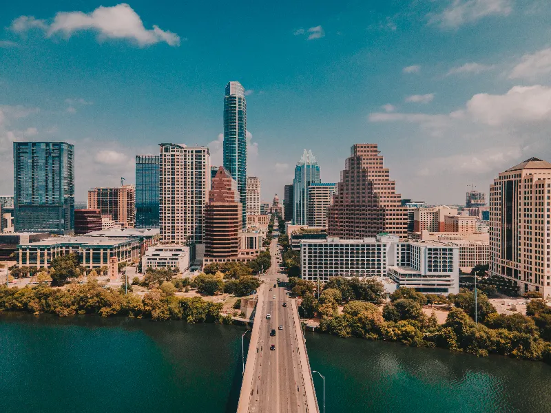 Downtown city skyline with a bridge over a river leading into tall buildings under a blue sky.